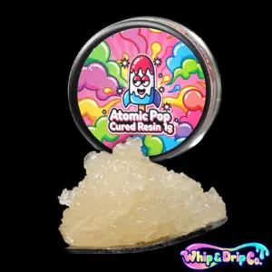 “Whip & Drip Co. Atomic Pop cured resin concentrate with golden extract displayed beside colourful candy-themed 1 gram product packaging on a black background.”