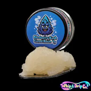 Whip & Drip Co. Blueberry Kush cured resin concentrate with pale golden extract displayed beside blueberry-themed 1 gram product packaging on a black background.