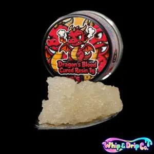 Whip & Drip Co. Dragons Blood cured resin concentrate with pale golden extract displayed beside dragon-themed 1 gram product packaging on a black background.