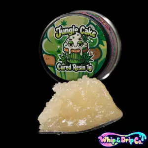 Whip & Drip Co. Jungle Cake cured resin concentrate with pale golden extract displayed beside jungle-themed cake-inspired 1 gram product packaging on a black background.