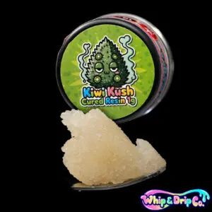 “Whip & Drip Co. Kiwi Kush cured resin concentrate with golden extract displayed beside kiwi-themed 1 gram product packaging on a black background.”