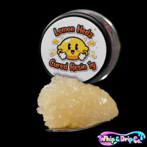 Whip & Drip Co. Lemon Hedz cured resin concentrate with pale golden extract displayed beside lemon-themed 1 gram product packaging on a black background.