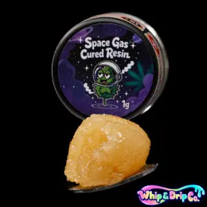 “Whip & Drip Co. Space Gas cured resin concentrate with pale golden extract displayed beside space-themed 1 gram product packaging on a black background.”