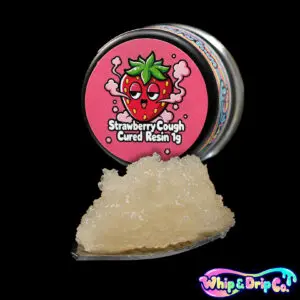 “Whip & Drip Co. Strawberry Cough cured resin concentrate with pale golden extract displayed beside strawberry-themed 1 gram product packaging on a black background.”