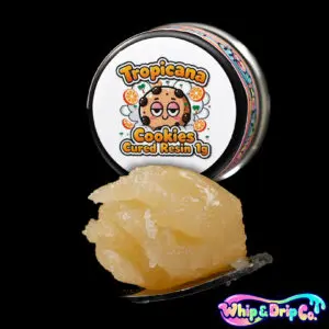 “Whip & Drip Co. Tropicana Cookies cured resin concentrate with golden extract displayed beside orange citrus-themed 1 gram product packaging on a black background.”