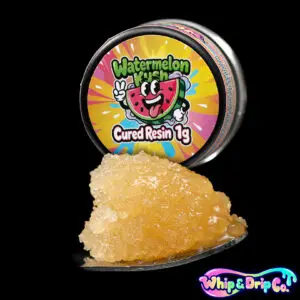 “Whip & Drip Co. Watermelon Kush cured resin concentrate with golden extract displayed beside colourful watermelon-themed 1 gram product packaging on a black background.”